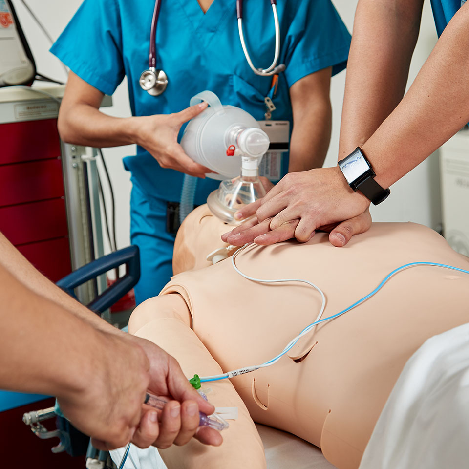 A medical team in blue scrubs simulates CPR on a medical dummy.